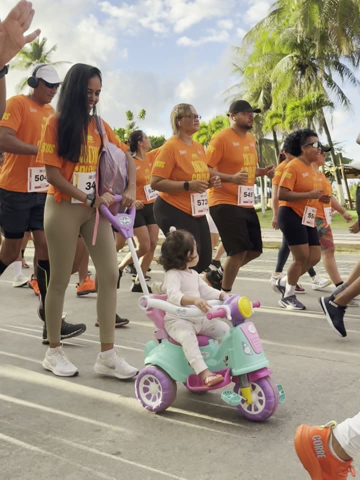 Corredores na pista, com uma criança de triciclo entre eles